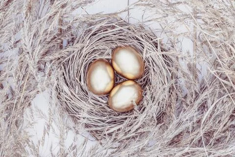 Golden eggs in a hay nest, Easter background, overhead view on white wooden.. Stock Photos