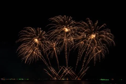 Golden Fireworks Exploding Over Dark Water At Night Long Exposure Shot Foto stock