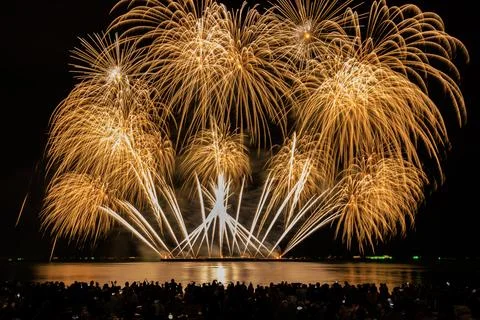 Golden Fireworks Exploding Over Sea With Silhouetted Crowd On Beach Wide An.. 库存照片