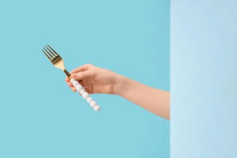 Golden fork with white beaded handle held by hand on blue background, kitchen Stock Photos