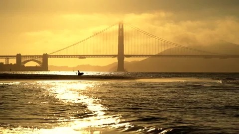 Golden Gate Bridge at sunset silhouetted with ocean waves and beach in fore.. Stock Footage 337602318
