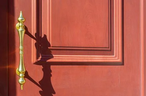 Golden handle casting shadow on red wood door Photos
