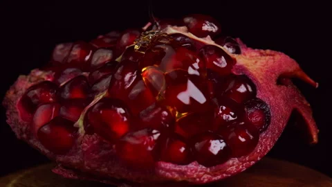 Golden honey dripping onto ruby pomegranate fruit and smoothly flowing down ripe Stock Footage 307802046