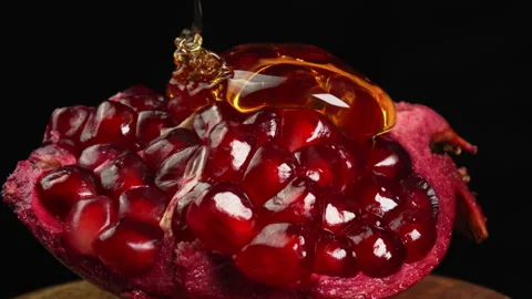 Golden honey dripping onto ruby pomegranate fruit and smoothly flowing down ripe Stock Footage 307818847