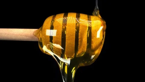 Golden honey smoothly flows down and around a wooden dipper against a plain Stock Footage 340952827