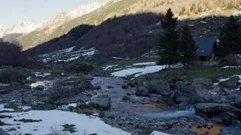 Golden hour illuminating river surface, snowy Pyrenees valley backdrop, rustic Stock Footage 306713530