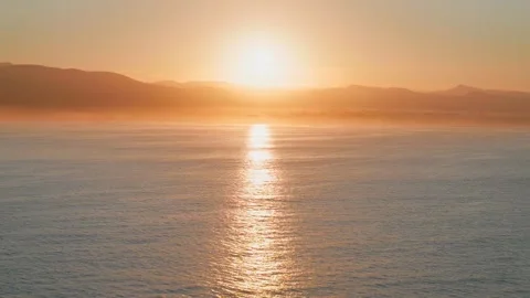 Golden hour sun setting over mountain ridge and ocean Stock Footage 338196881