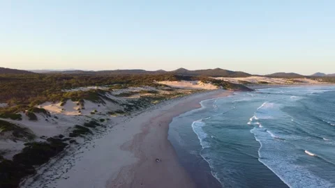 Golden hour sunset flight over coastal dunes and ocean waves in Anna Bay, Au Stock Footage 345149431