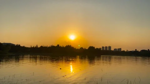 Golden hour sunset reflecting over a lake with distant city skyline silhouettes Stock Footage 342330236