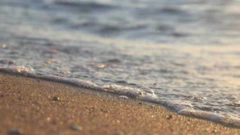 Golden hour waves gently washing onto textured wet beach sand Stock Footage 337418364