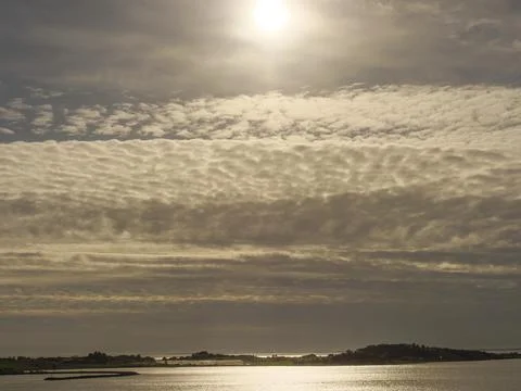 A golden illuminated sky with dramatic cloud formations reflected in the calm Stock Photos