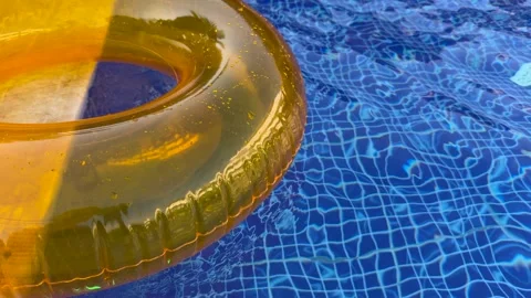 Golden inflatable ring floats on blue pool water, drifting beside sunlit ripples Stock Footage 345652222