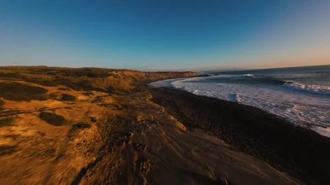 Golden light bathes coastal cliffs and dark beach Stock Footage 339788710