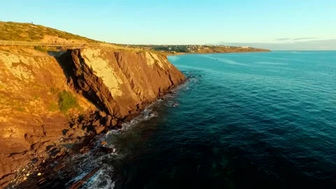 Golden light on rugged cliffs at sunset next to a calm rich blue ocean aerial Stock Footage 262287889