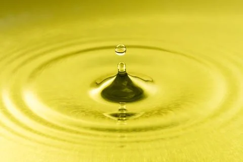 Golden liquid drop creating ripples on a yellow surface Stock Photos