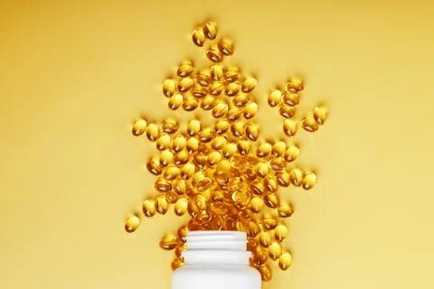 Golden Omega-3 fish oil capsules poured out of a jar on a yellow background Stock Photos