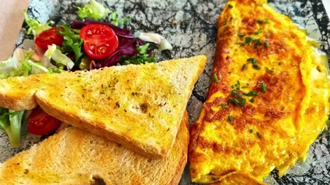 Golden omelette served with toasted bread and a fresh salad mix, captured on a Stock Footage 325685638