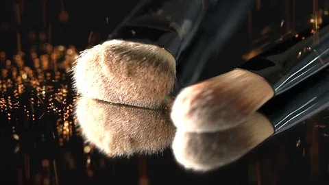 Golden orange glitter falling on the makeup brushes on the mirror on the black Stock Footage 75971041
