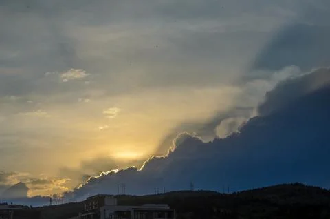 Golden rays pierce through clouds as the sun bids farewell over the hillsid.. Stock Photos