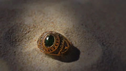 Golden Ring with Green Emerald Cut Gem in the Sand Stock Footage 147983477