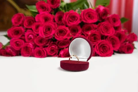 Golden ring in a red gift box and a large bouquet of roses in the background. Stock Photos
