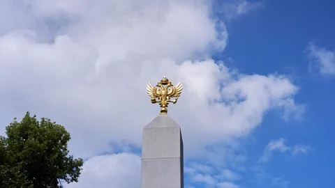 Golden Russian double-headed eagle atop a tall granite obelisk Stock Photos