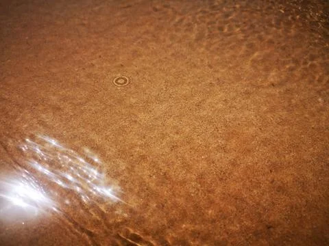 Golden sand can be seen through the water with a beautiful pattern. Stock Photos