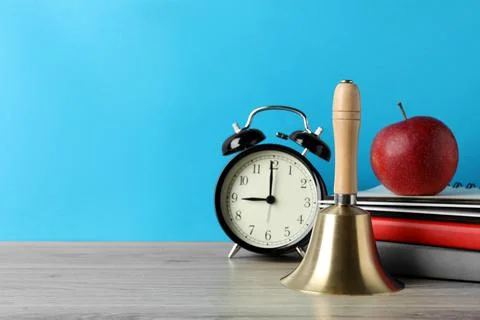Golden school bell, apple, alarm clock and books on wooden table against turq Stock Photos