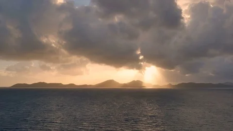 Golden setting sun casts rays under dark clouds Caribbean island view from ocean Stock Footage 78937511