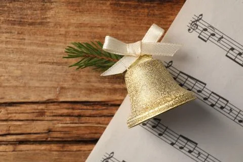 Golden shiny bell with bow and music sheet on wooden table, flat lay. Space.. Stock Photos