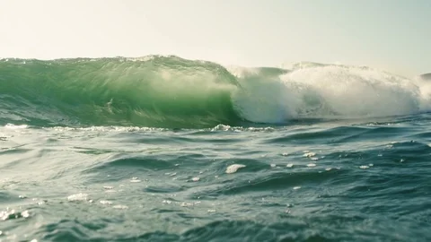 Golden small wave breaking with surfer in the back Stock Footage 128184339