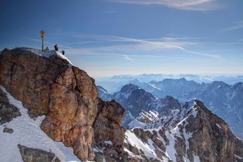 Golden summit cross and tiny climbers on top of Zugspitze peak Stock Photos