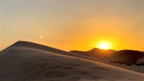 Golden sun dips behind smooth dunes casting long soft shadows across desert sand Stock Footage 288726296