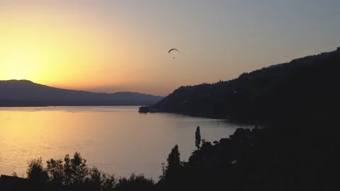 Golden sun dips low over calm lake waters as Paraglider flies by Stock Footage 343881142