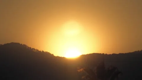 Golden sun disk emerging above silhouetted hills and tree line, casting warm Stock Footage 329622583