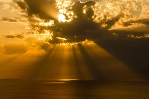 Golden sun rays breaking through dramatic clouds at sea. Stock Photos