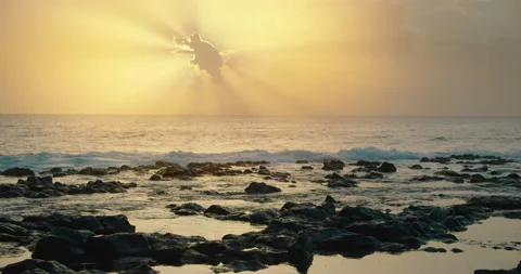 Golden sun rays emerge through the clouds over the sea. Ocean waves splash on Stock Footage 233223148