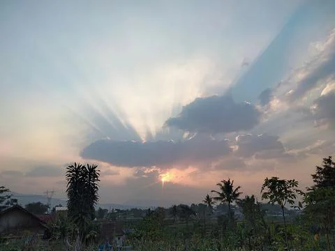 Golden Sun Rays Piercing Clouds Over Rural Village at Sunset Stock Photos