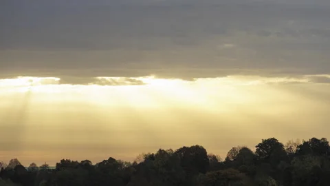 Golden sun rays shining through clouds above a forest time lapse Stock Footage 221791016