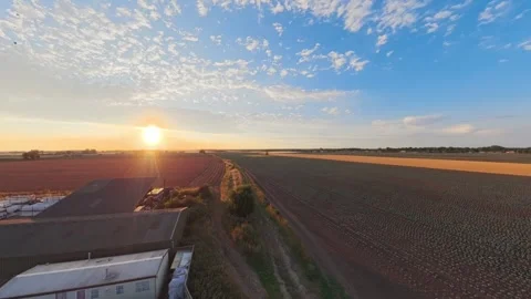 Golden sun sets over open fields and rural structures 库存影片 342556573