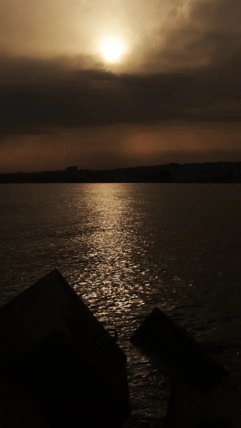 Golden sun setting behind clouds over calm sea with breakwater blocks Stock Footage 344880207