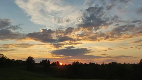 Golden sun setting behind dark forest under a blue sky Stock Footage 335717165