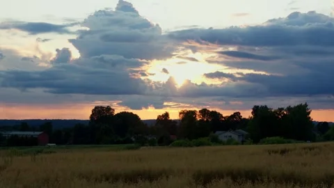 Golden sun setting behind dramatic clouds over agricultural field and rural Stock Footage 342027946