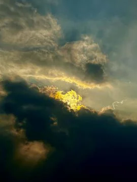 Golden sunlight breaking through dark dramatic storm clouds in atmospheric Stock Photos