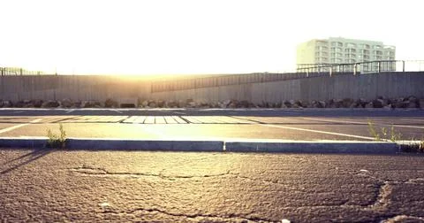 Golden sunlight illuminates an empty parking lot at dusk near buildings Ilustración de archivo
