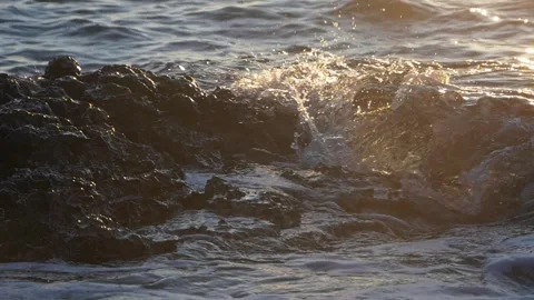Golden sunlight illuminates ocean waves splashing over dark rocky coast. Stock Footage 337410383