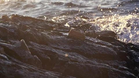 Golden sunlight illuminates sparkling ocean waves crashing onto rocky coast Stock Footage 337409940