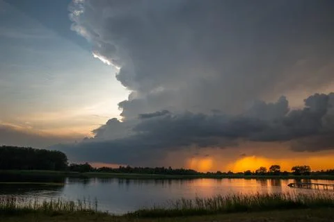 Golden Sunset and Approaching Massive Storm Clouds Over Lake Shore Stock Photos