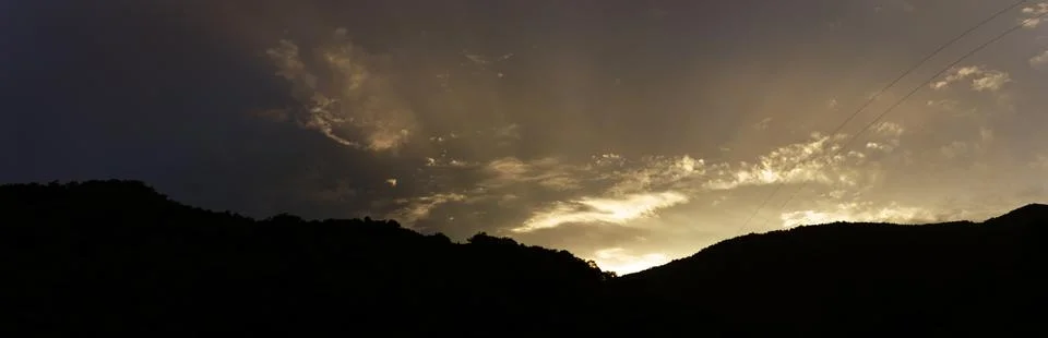 Golden sunset casting dramatic light over mountain ridge with scattered clo.. Stock Photos
