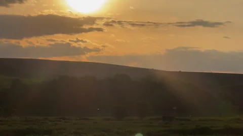 Golden sunset casting sun rays over green hills Vidéo 340237758